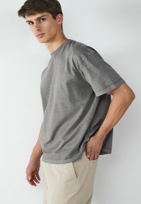 Szara bawełniana koszulka z krótkim rękawem, luźny krój, subtelna faktura, w zestawieniu z jasnobeżowymi spodniami, posiadającymi boczne kieszenie.