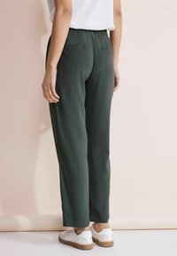Pantaloni verdi, leggeri, con vita elastica e design a gamba dritta, due tasche posteriori e lunghezza alla caviglia, abbinati a sneakers bianche.