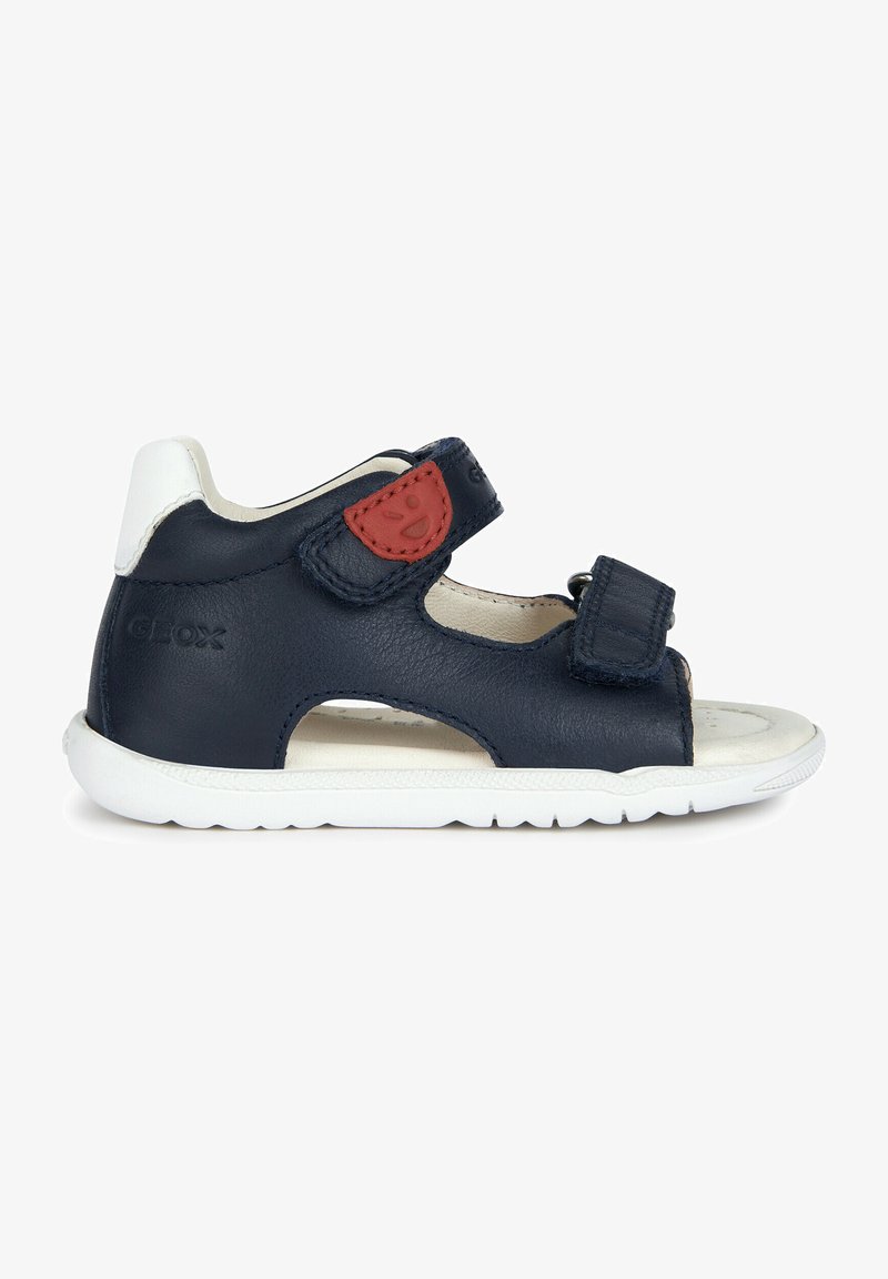 Sandalo in pelle blu navy con suola bianca, dotato di due cinturini in Velcro e un accento rosso. Design aperto con ritagli per la traspirabilità.