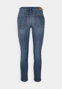 Denimjeans i mörkblått med tapered ben, två bakfickor och en läderetikett i midjan. Ytan är slät och ren.