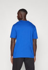 T-shirt bleu à manches courtes en tissu coton doux avec un col rond. Texture lisse, coupe décontractée. Pas de motifs ni de métal visibles.