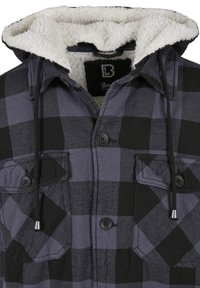 Rutigt skjorta i svart och grått med en huva i syntetpäls. Har knäppt fram, två bröstfickor och justerbara dragsnören.