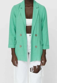 Mintgroene dubbelbreasted blazer met twee bruine knopen, driekwartmouwen en een lichtgewicht gestructureerde stof. Gecombineerd met witte verouderde jeans.