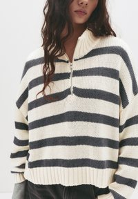 Gestreifter Strickpullover in Creme und Marineblau. Mit einem Halb-Reißverschluss-Kragen, elastischem Saum und lockeren Ärmeln. Texturiert, leichtes Material.
