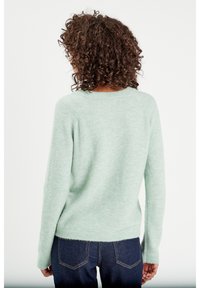 Suéter verde menta hecho de un tejido suave y texturizado. Presenta un cuello redondo y mangas largas, con un corte relajado y bajo acanalado.