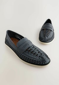 Mocasines grises con textura trenzada, diseño sin cordones y suela blanca contrastante. Incluye dos pares colocados uno al lado del otro.