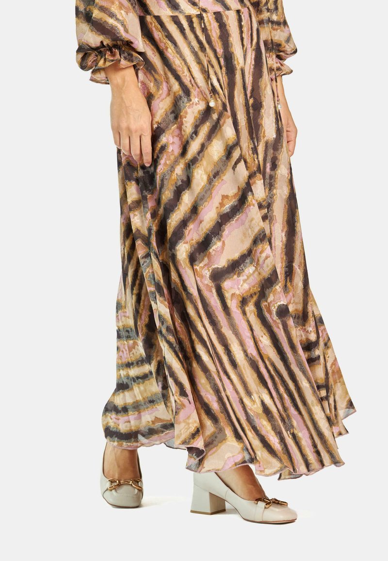 Vestido maxi con un patrón ondulado en rosa, marrón y dorado, con mangas largas y un diseño fluido, combinado con unos zapatos de tacón beige que tienen un lazo decorativo.