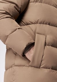 Giacca imbottita marrone con tessuto liscio, tasca laterale e design a trapuntatura con cuciture pronunciate.