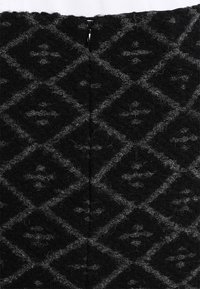 Černý látkový materiál s šedým diamantovým vzorem, který má texturovaný povrch. Kovový zip je umístěn ve středu zad.