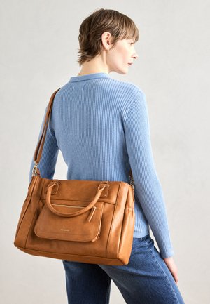 Tan leather handbag with an exterior zip pocket, dual handles, and adjustable shoulder strap, paired with a light blue ribbed sweater and jeans.