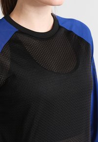 Maglietta sportiva nera in rete con accenti blu sulle maniche. Caratterizzata da un collo rotondo e un tessuto testurizzato per la traspirabilità.