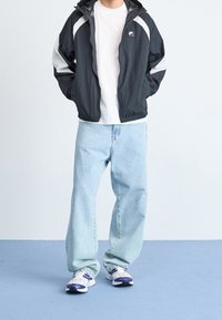 Musta ja harmaa hupullinen tuulitakki, valkoinen t-paita, vaaleansiniset väljästi istuvat farkut ja valkoiset lenkkarit, joissa on violetteja yksityiskohtia.