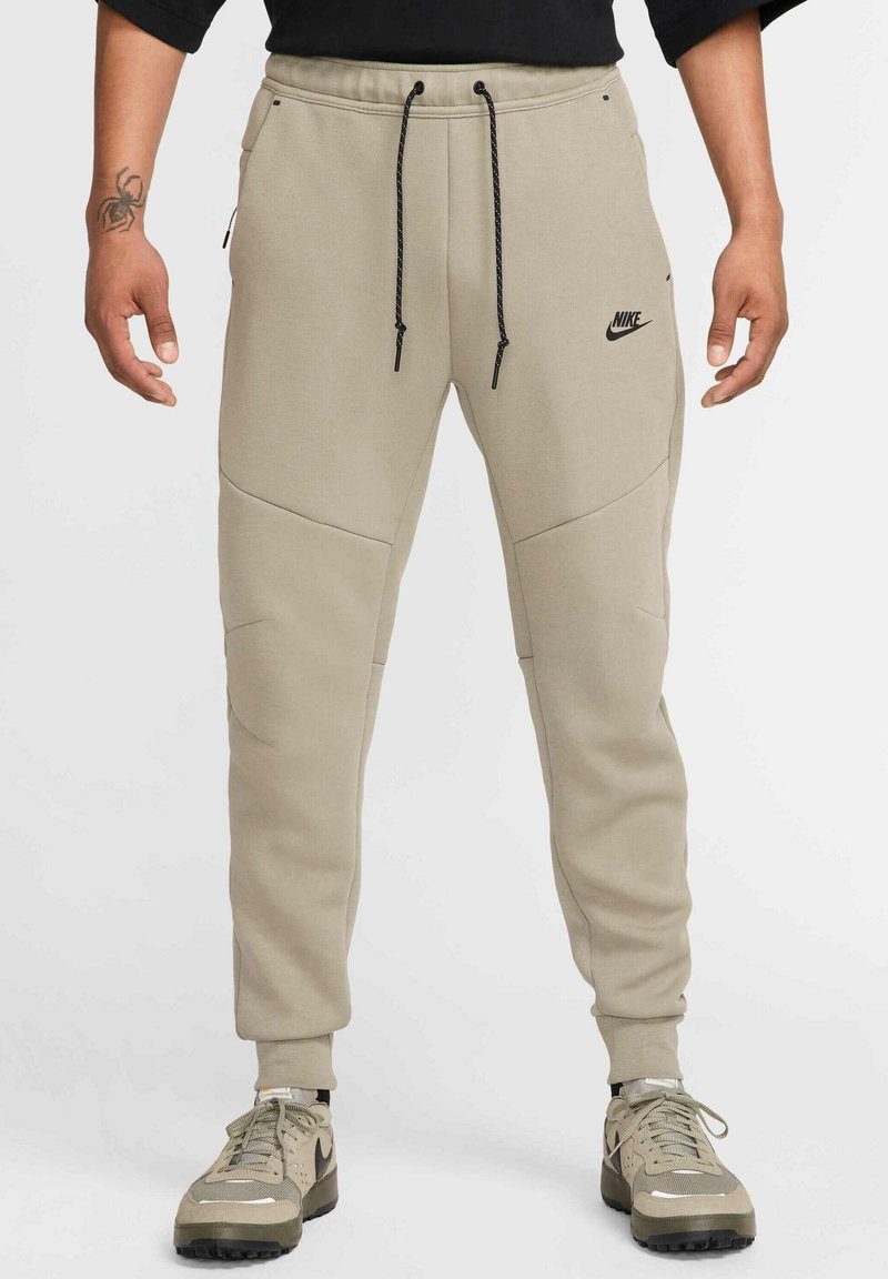 Beige Nike Jogginghosen mit elastischem Bund und schwarzen Kordeln, ausgestattet mit schrägen Seitentaschen und dezenten Nähten.