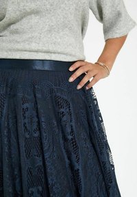 Gonna in pizzo blu navy con intricate fantasie floreali, texture semi-trasparente e cintura in satin. Il look completo include un top grigio.