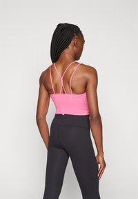 Fialový športový crop top so štíhlymi krížovými ramienkami na chrbte. Čierne legíny s vysokým pásom a hladkým povrchom.
