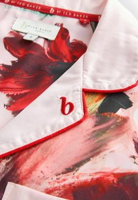 Zijde blouse met een bloemenpatroon in rode en roze tinten, met een rode rand op de kraag en een geborduurd logo in rood.