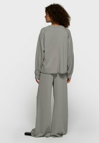 Sweatshirt gris clair surdimensionné avec manches raglan, associé à un pantalon large assorti, tous deux en tissu doux et texturé.