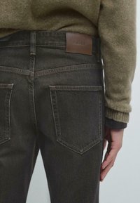 Jeans in denim scuro con una finitura testurizzata, dotati di due tasche posteriori e di un'etichetta in pelle con la scritta "Massimo Dutti" sulla cintura.