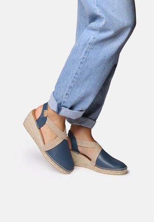 Blue leather wedge shoes with a woven natural rope sole and elastic crisscross straps. Stylish open-back design complements casual denim.