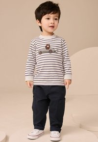 Cămașă în dungi cu mânecă lungă, brodată cu o mașină și un urs, purtată cu pantaloni cargo bleumarin și adidași albi. Textură de bumbac fin.