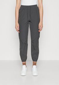 Harmaat cargo-housut, joissa on joustava vyötärö, sivutaskut ja joustavat hihnat. Yhdistetty valkoisiin lenkkareihin ja ruskeisiin nilkkasukkasiin.