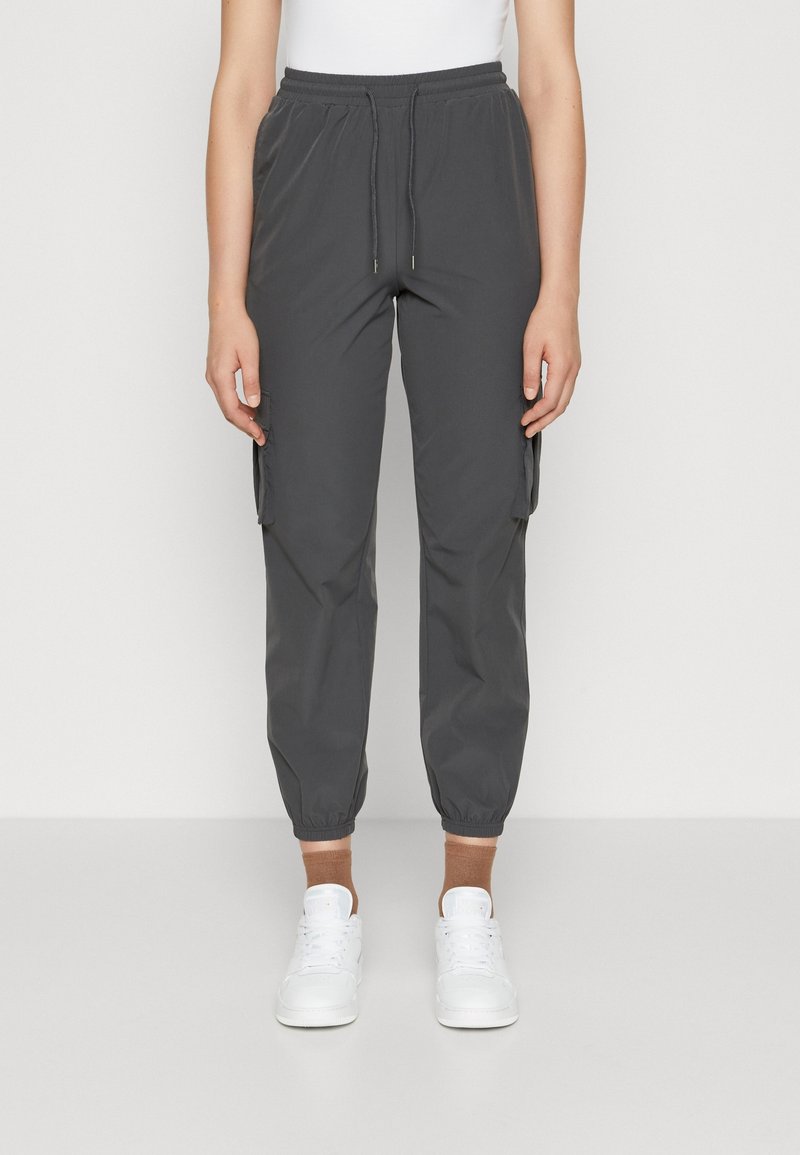 Harmaat cargo-housut, joissa on joustava vyötärö, sivutaskut ja joustavat hihnat. Yhdistetty valkoisiin lenkkareihin ja ruskeisiin nilkkasukkasiin.