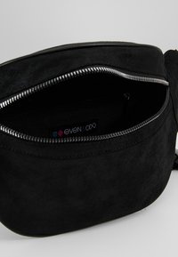 Borsa pochette in suede nero con una zip argentata parzialmente aperta che rivela un'etichetta in tessuto all'interno.