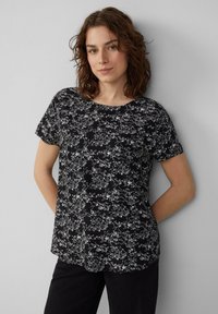 Zwart t-shirt met korte mouwen en witte bloemenprint, ronde halslijn en ontspannen pasvorm. Glad textuur met een zachte val en afgeronde onderkant.
