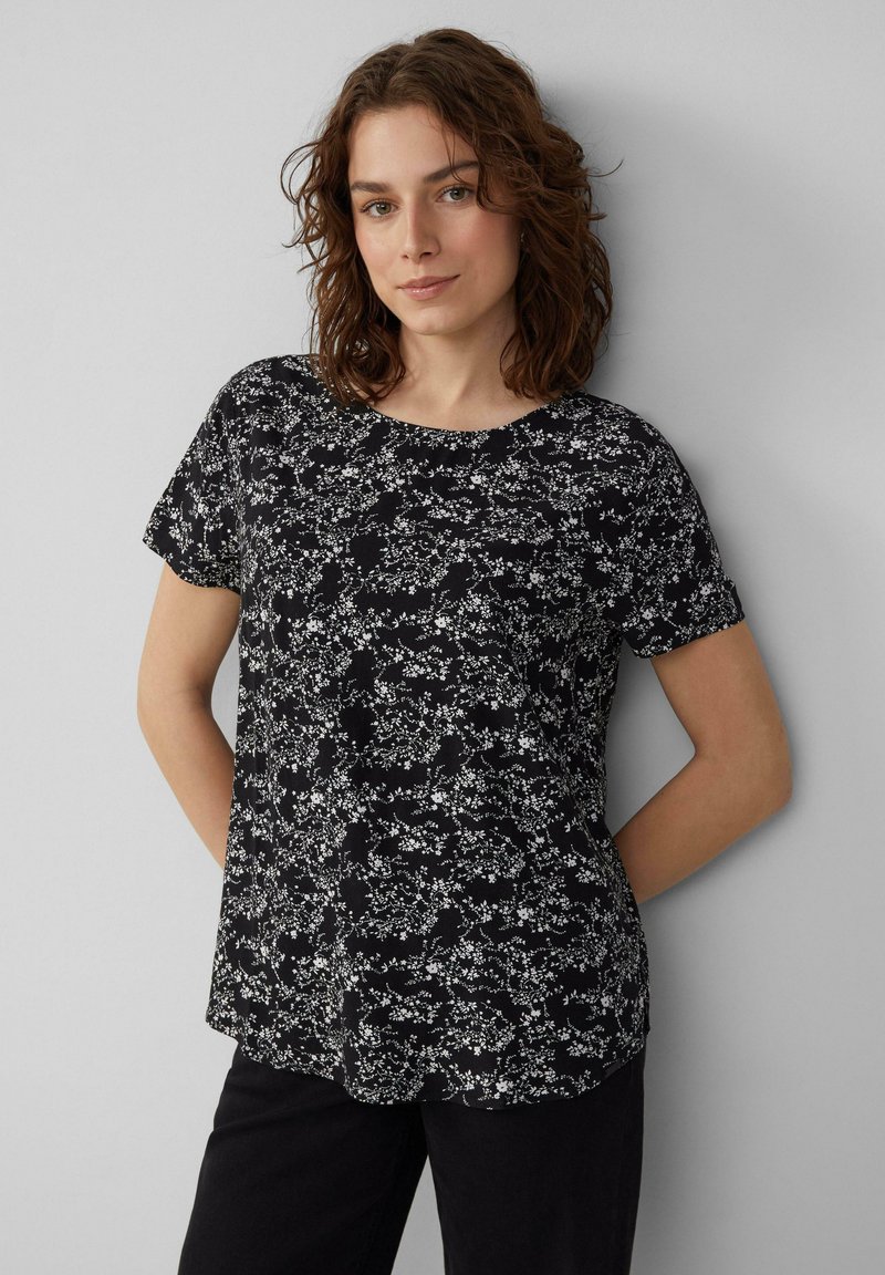 Schwarzes Kurzarmoberteil mit weißen Blumenmuster, runder Halsausschnitt und lässigem Schnitt. Glatte Textur mit sanftem Fall und abgerundetem Saum.