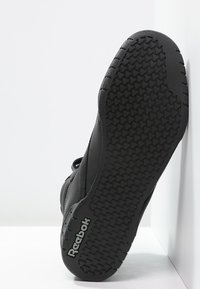 Baskets noires avec une semelle en caoutchouc texturée, dotées d'un motif en losanges pour une meilleure adhérence, et d'un logo embossé sur le côté, conçues pour le confort et le soutien.