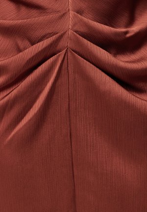 Roostevärvi kangas, millel on peen vertikaalne tekstuur ja kogutud, volditud detailid, mis loovad sümmeetrilise, kalasaba meenutava mustri.