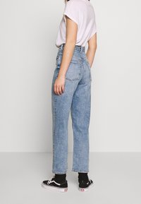 Jeans azzurri chiari a vita alta con una vestibilità affusolata, tasche frontali e posteriori, cuciture a vista e orli sfrangiati, abbinati a sneaker nere.