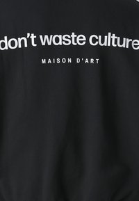 Schwarzer Pullover mit auffälligem weißem Text: "don't waste culture" und "MAISON D'ART." Glatte Textur, lässiges Design und entspannte Passform.