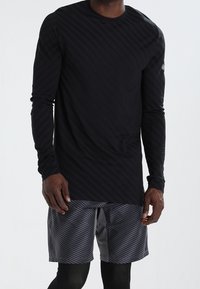 Musta pitkähihainen urheilupaita, jossa on vinot raidat, yhdistettynä harmaisiin kuvioituihin shortsihin; molemmat on valmistettu kevyestä ja hengittävästä kankaasta.