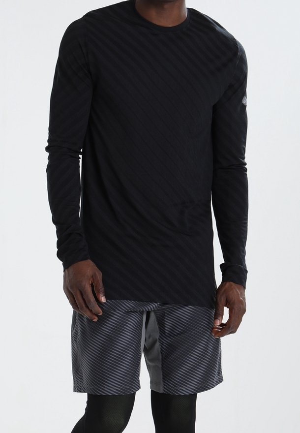 Langärmliges schwarzes Sporthemd mit diagonalen Streifen, kombiniert mit grauen gemusterten Shorts; beide aus leichtem, atmungsaktivem Material hergestellt.