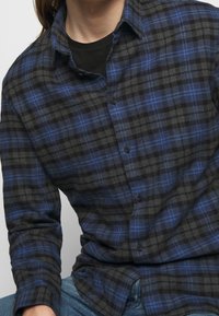 Svart och blå rutigt skjorta med knäppning, med långa ärmar och en mjuk textur. Synliga knappar och en krage.