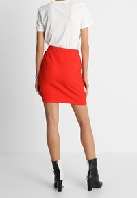 Krátká červená sukně s texturovanou tkaninou, kombinovaná s bílým tričkem a černými kotníkovými botami. Sukně má přiléhavý střih a délku nad kolena.