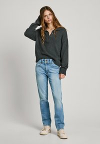 Tumehall villane sviiter, millel on henley krae ja teemantmuster, koos helesiniste sirgete pükste ja beežide jooksukingadega.