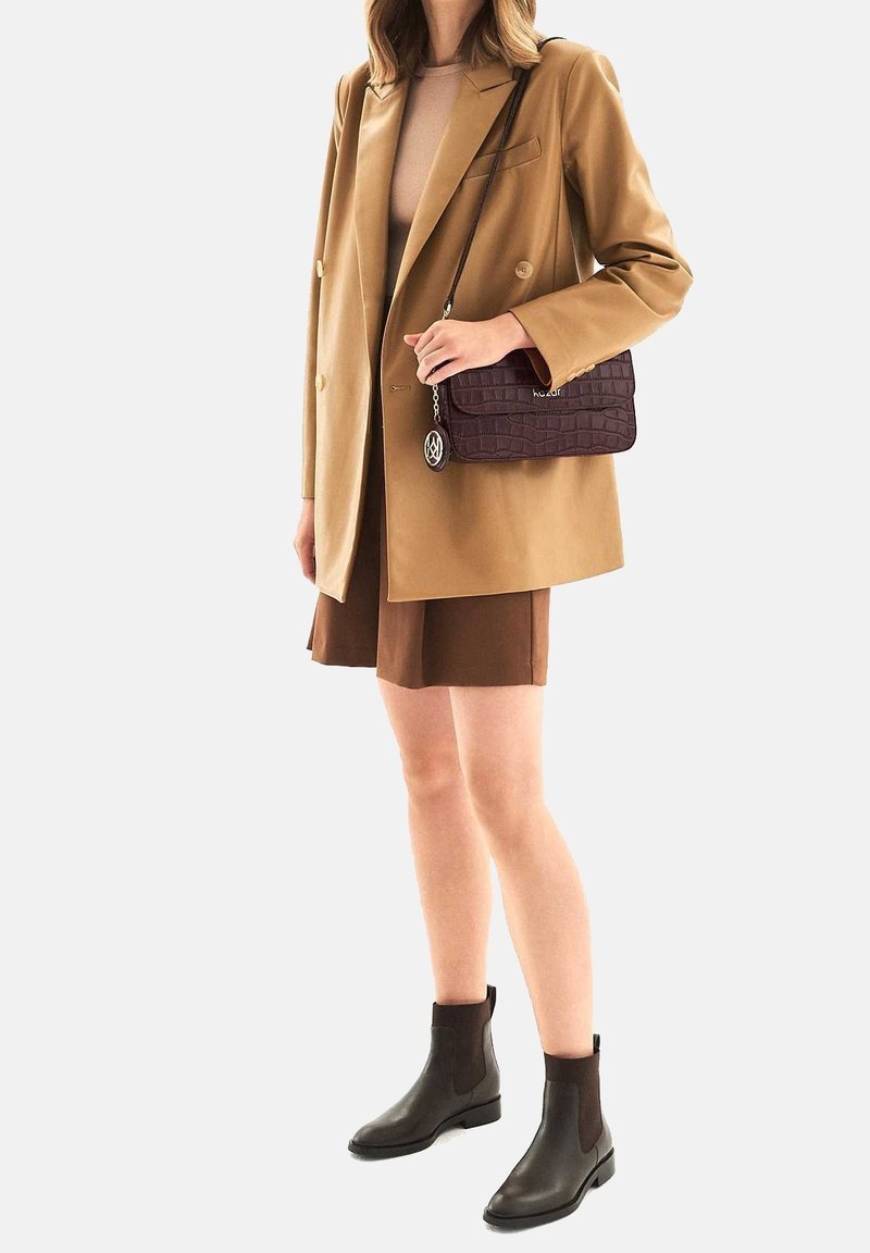 Blazer beige de doble botonadura sobre una blusa color marrón claro, combinado con pantalones cortos marrones. Botines oscuros marrones y un bolso texturizado de color púrpura oscuro.