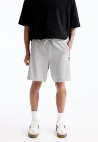Shorts en coton gris avec une taille élastique et un cordon de serrage, dotés de poches latérales et d'une coupe décontractée. Associés à un haut oversize noir.