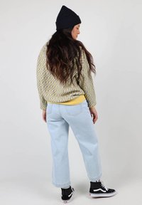 Pull à motifs jaune et gris, jean taille haute bleu clair, baskets noires avec accents blancs, et un bonnet noir.