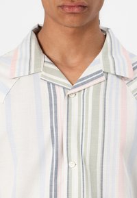 Camisa de manga corta a rayas en colores claros: blanco, verde, azul y rosa. Presenta un collar y un solo botón en el frente. Tejido texturizado.