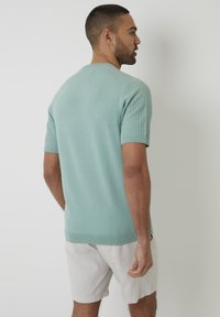 Licht mintgroen gebreid short-sleeve sweater met een textuurpatroon op de mouwen en een geribbelde onderrand, gecombineerd met lichtgekleurde shorts.