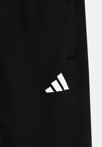 Svarta träningsbyxor i mjukt material, med en vit Adidas-logotyp i ett diagonalt randmönster på underbenet.