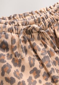 Tissu beige avec imprimé léopard marron et gris, doté d'une ceinture élastique et d'un cordon noué.