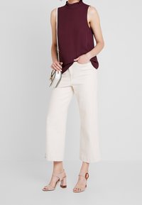 Top senza maniche color borgogna con colletto arricciato, abbinato a pantaloni larghi color crema. Tacchi rosa chiaro con dettaglio trasparente e accentuazione circolare.