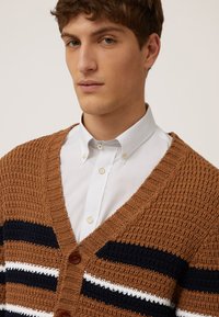 Brun, stickad cardigan med v-ringning, med vertikala marinblå och vita ränder, träknappar och en texturerad väv.