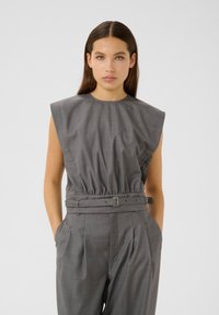 Jumpsuit grigio senza maniche con vita arricciata e dettaglio della cintura. Tessuto liscio con una texture sottile, con ampie spalline e tasche.