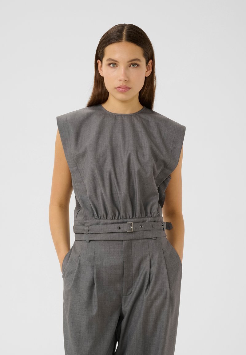 Jumpsuit grigio senza maniche con vita arricciata e dettaglio della cintura. Tessuto liscio con una texture sottile, con ampie spalline e tasche.