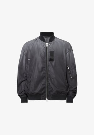 Chaqueta bomber negra hecha de un suave material satinado. Presenta un cierre frontal con cremallera, puños acanalados y dos bolsillos laterales con un detalle de parche.